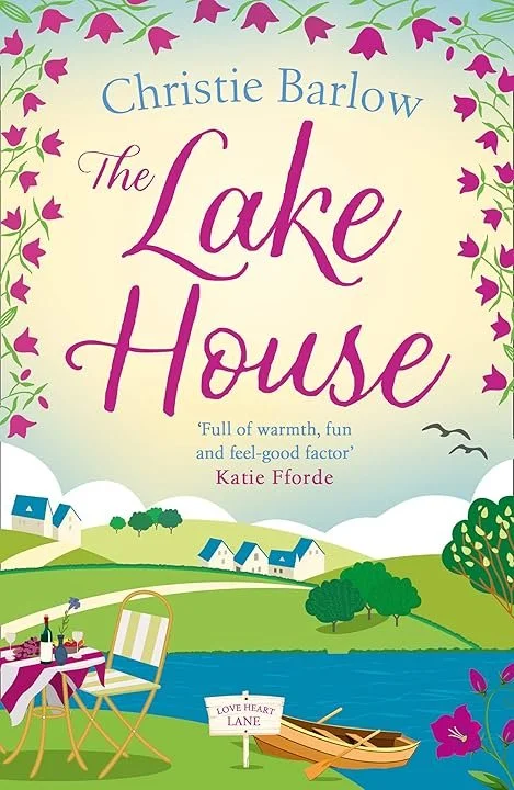 Book cover for 'The Lake House' by Christie Barlow, featuring a scenic illustration of a lake, green hills, houses, trees, a picnic table, and a boat with a sign that says 'Love Heart Lane.'