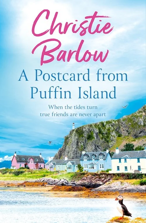 Book cover titled 'A Postcard from Puffin Island' by Christie Barlow, featuring colourful houses along the coastline, a grassy cliff with a lighthouse, and a puffin holding a postcard sitting near the water.