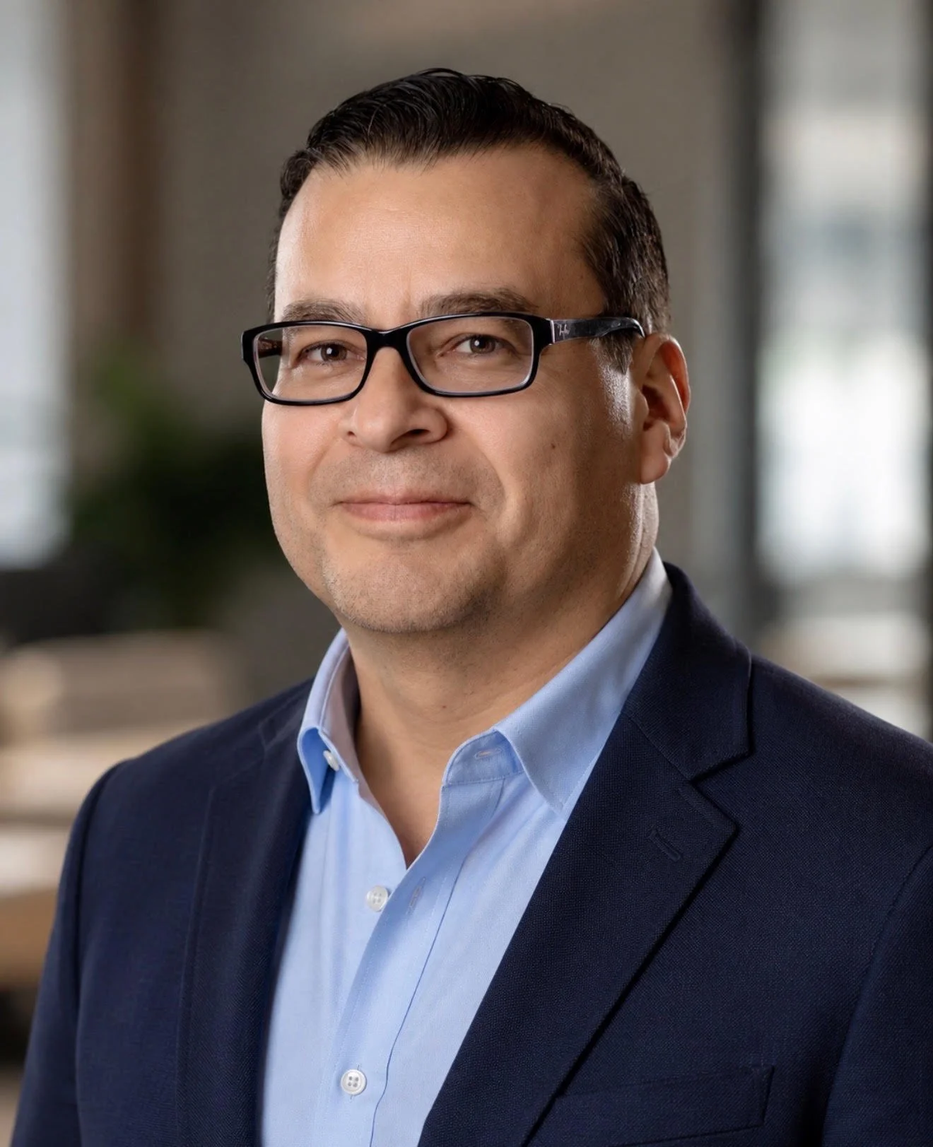 Portrait of a man in business attire, wearing glasses, with a neutral background.