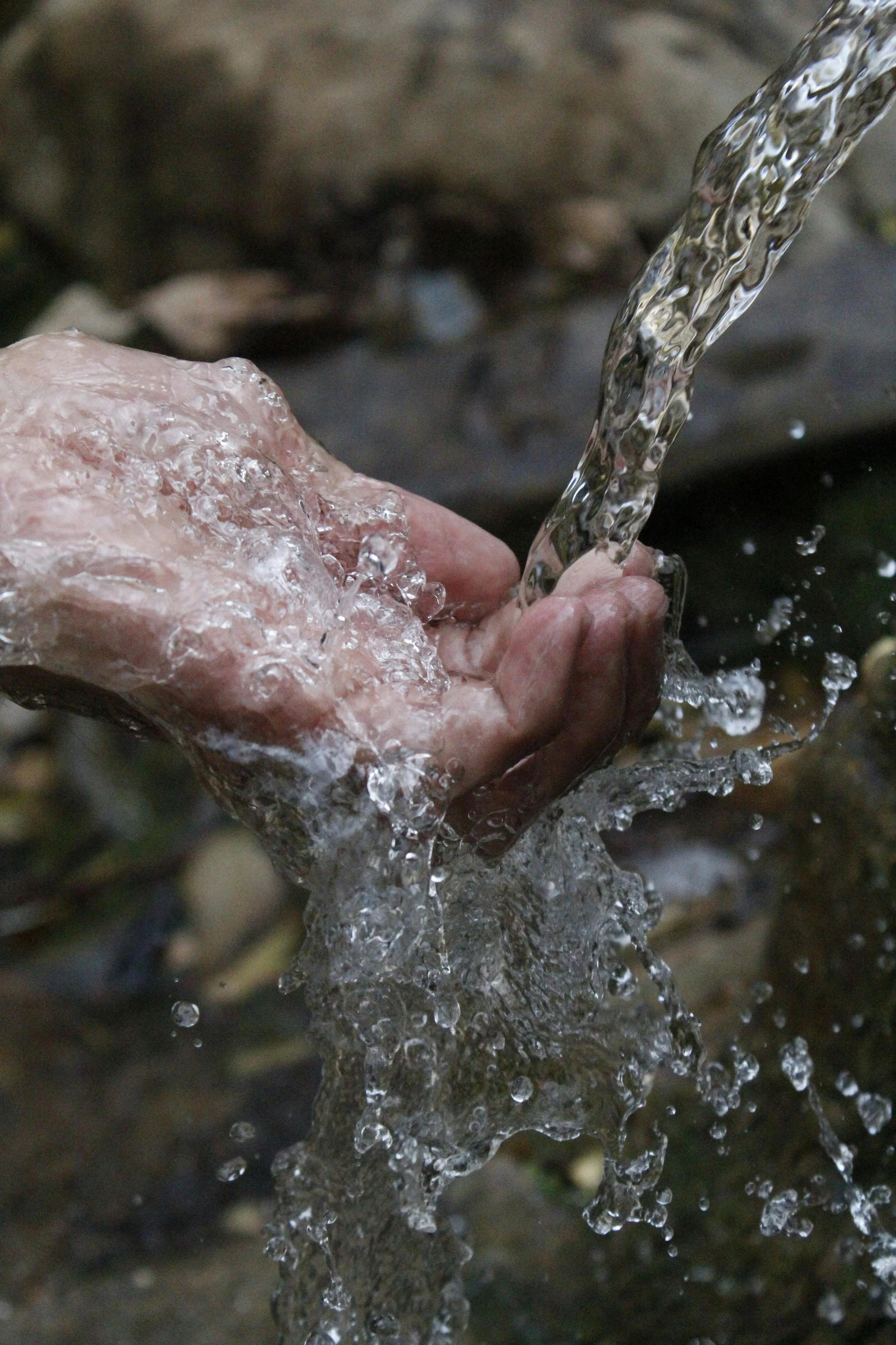 A person's hand holding flowing water over rocks outdoors.