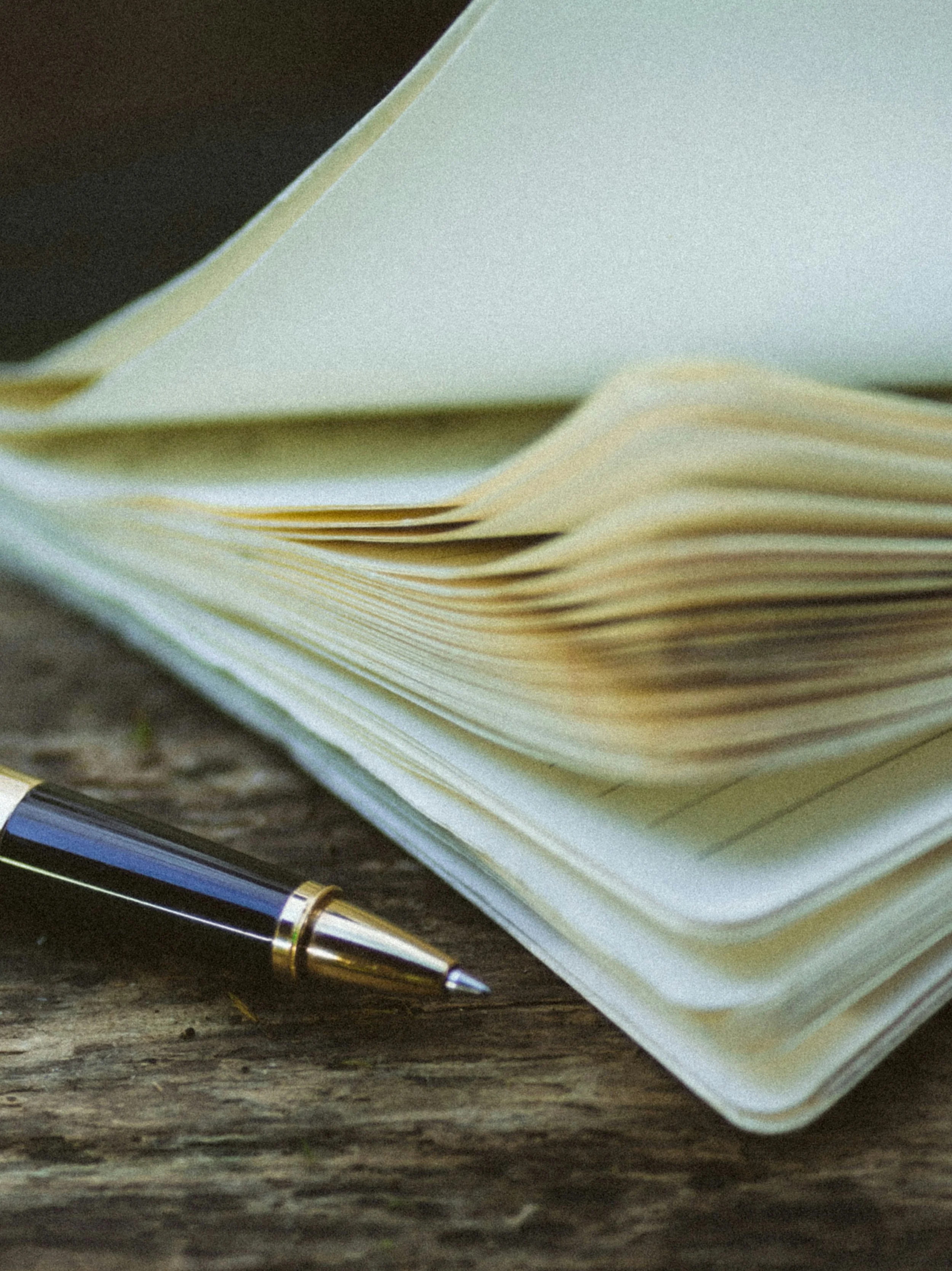 An open notebook with cream-colored pages, a black and gold pen resting on a wooden surface.
