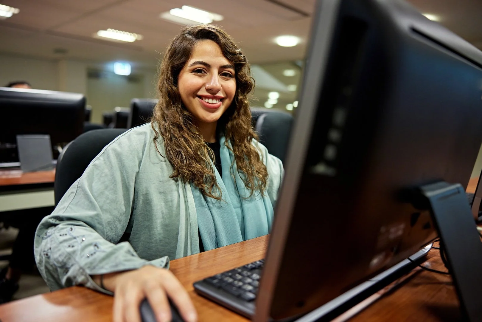 A smiling young student while studying in her laptop in the University's library.