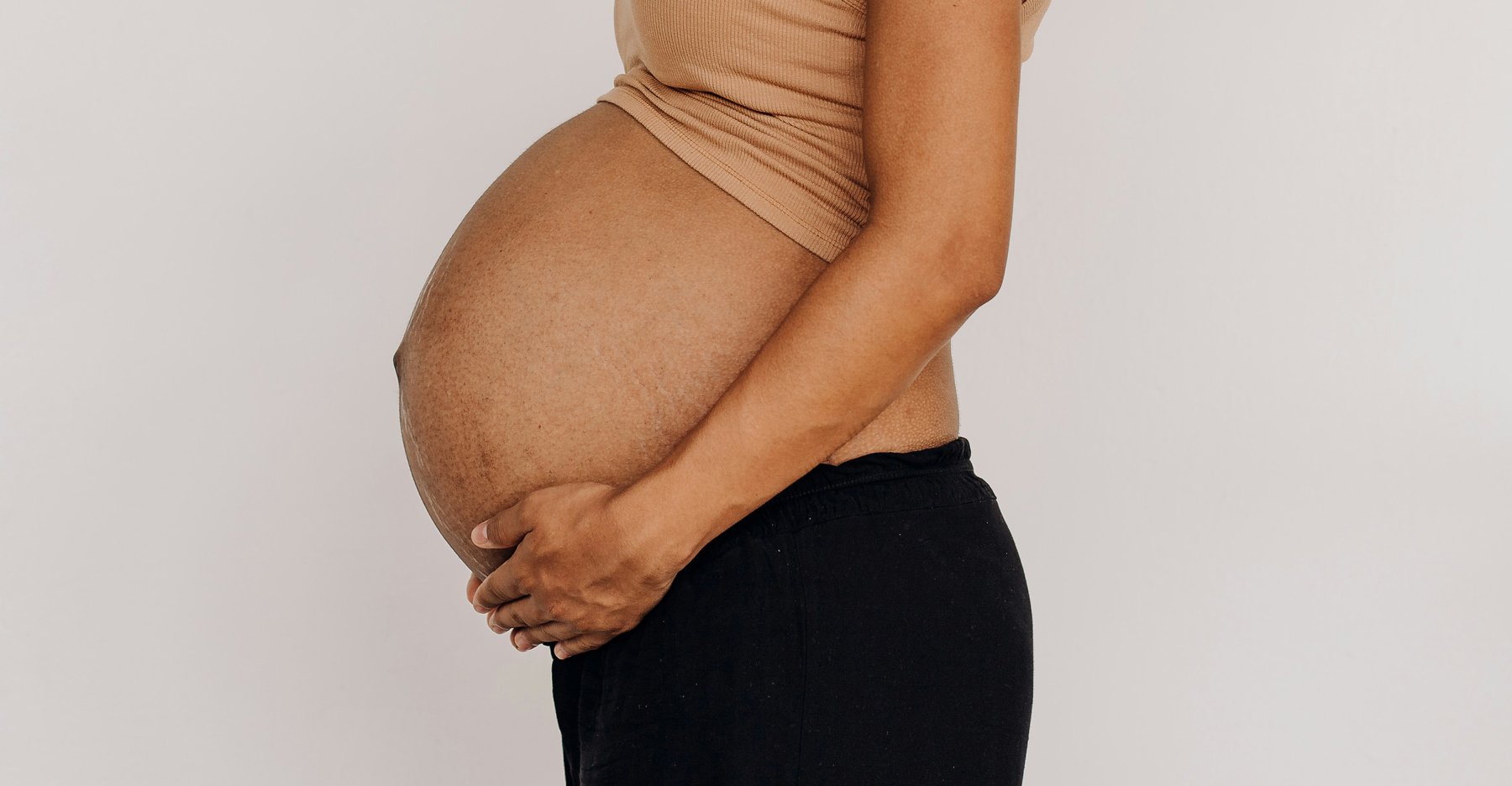 A women of color holds under her pregnant belly, choosing a home birth with a midwife and doula team.