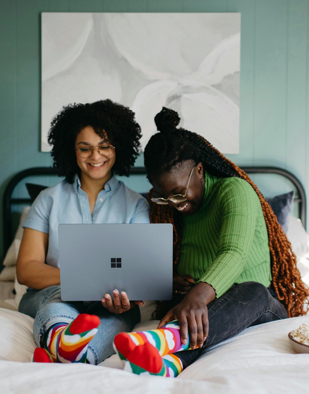 Two women of color sit on their bed on their computer. They are undergoing virtual doula pregnancy and labor support.