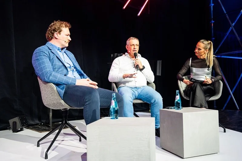 Katharina Aguilar moderiert einen Talk mit zwei Gästen in Sesseln auf der Bühne der RetailNXT