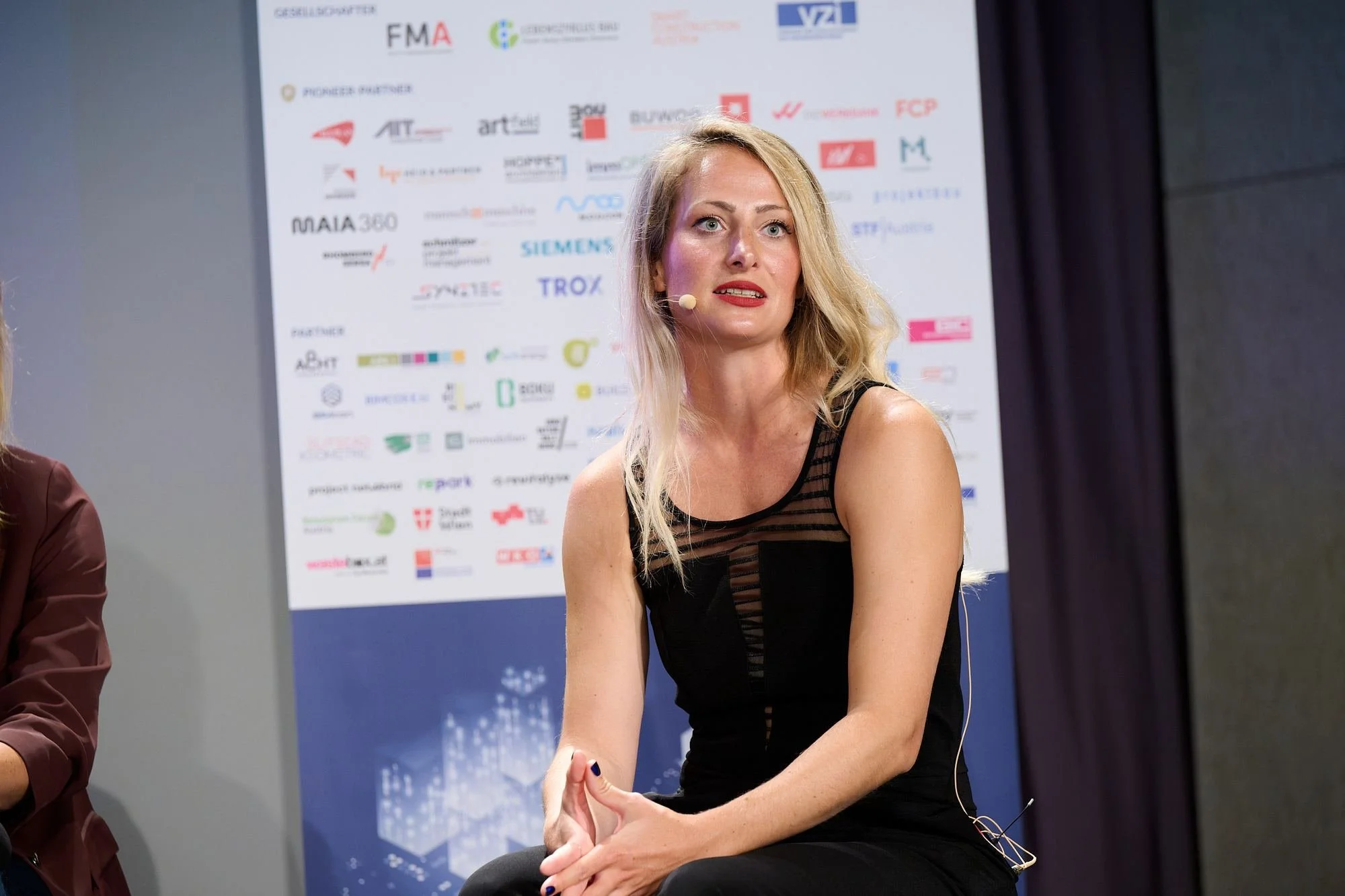 Katharina Aguilar sitzt auf dem Podium des Innovationskongresses vor der Partnerwand von Digital Findet Stadt