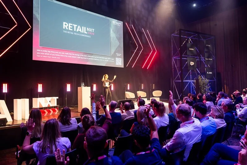 Moderatorin Retail Katharina Aguilar eröffnet die Main Stage der RetailNXT 2026 in Bad Vilbel, das Publikum hebt die Hände