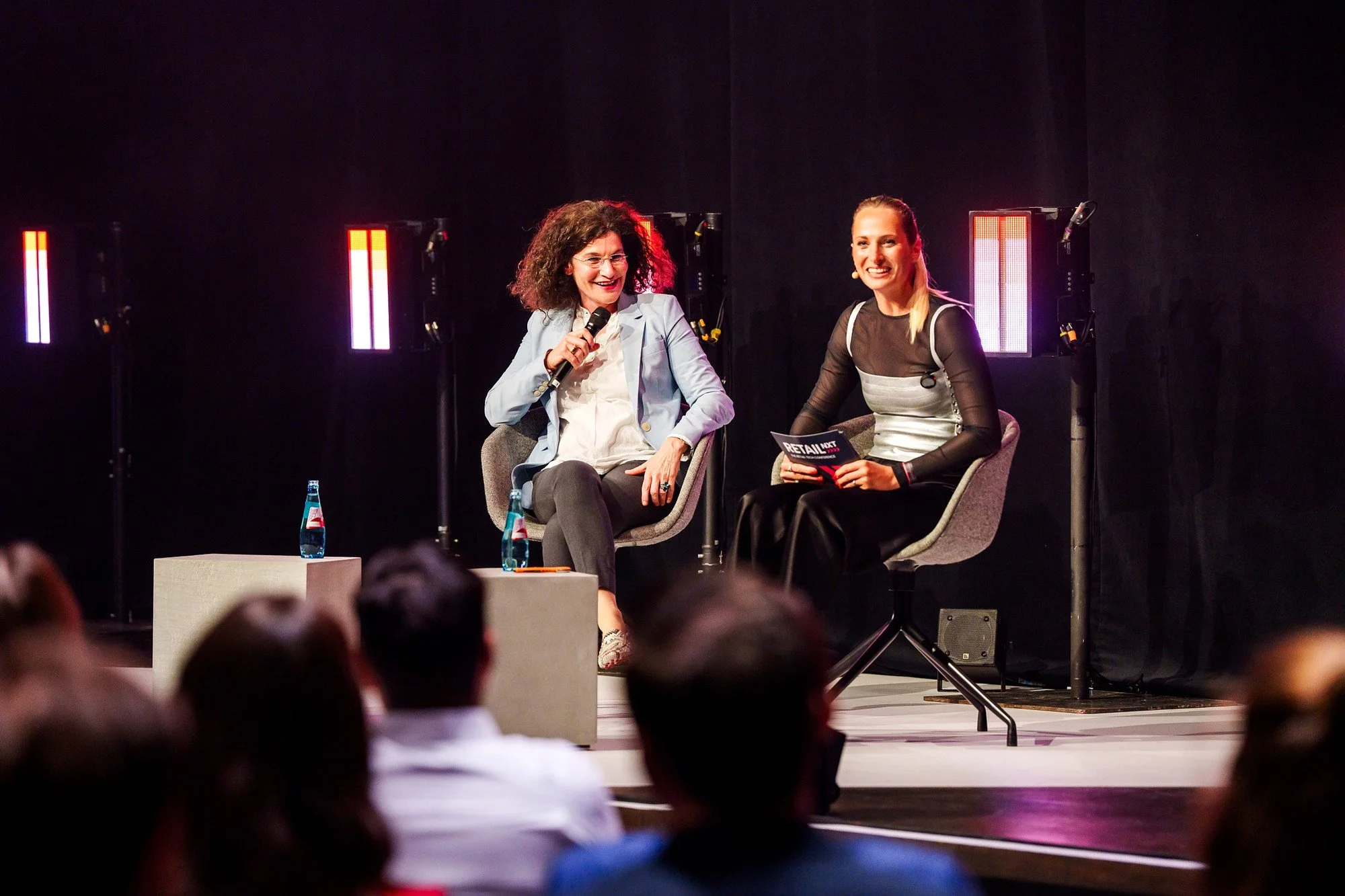 Weleda-CEO Tina Müller lacht im Fireside Chat mit Moderatorin Katharina Aguilar auf der RetailNXT 2026 in Bad Vilbel