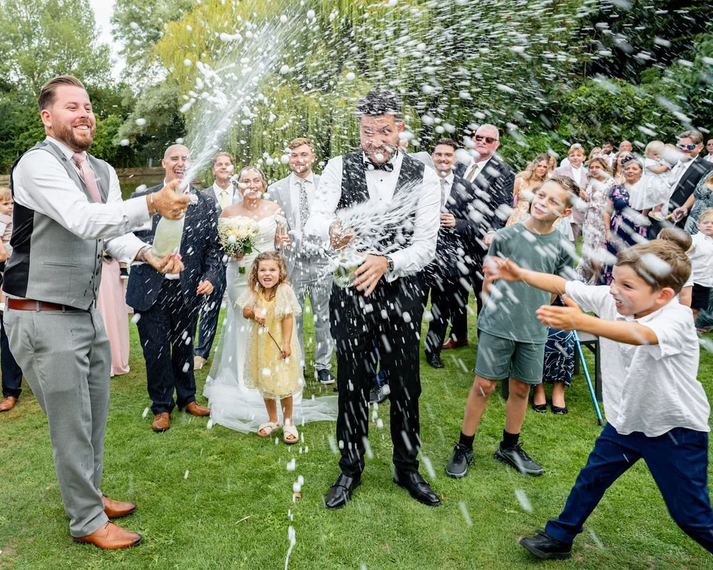 Celebration during a wedding with guests splashing champagne on the bride and groom in a garden.