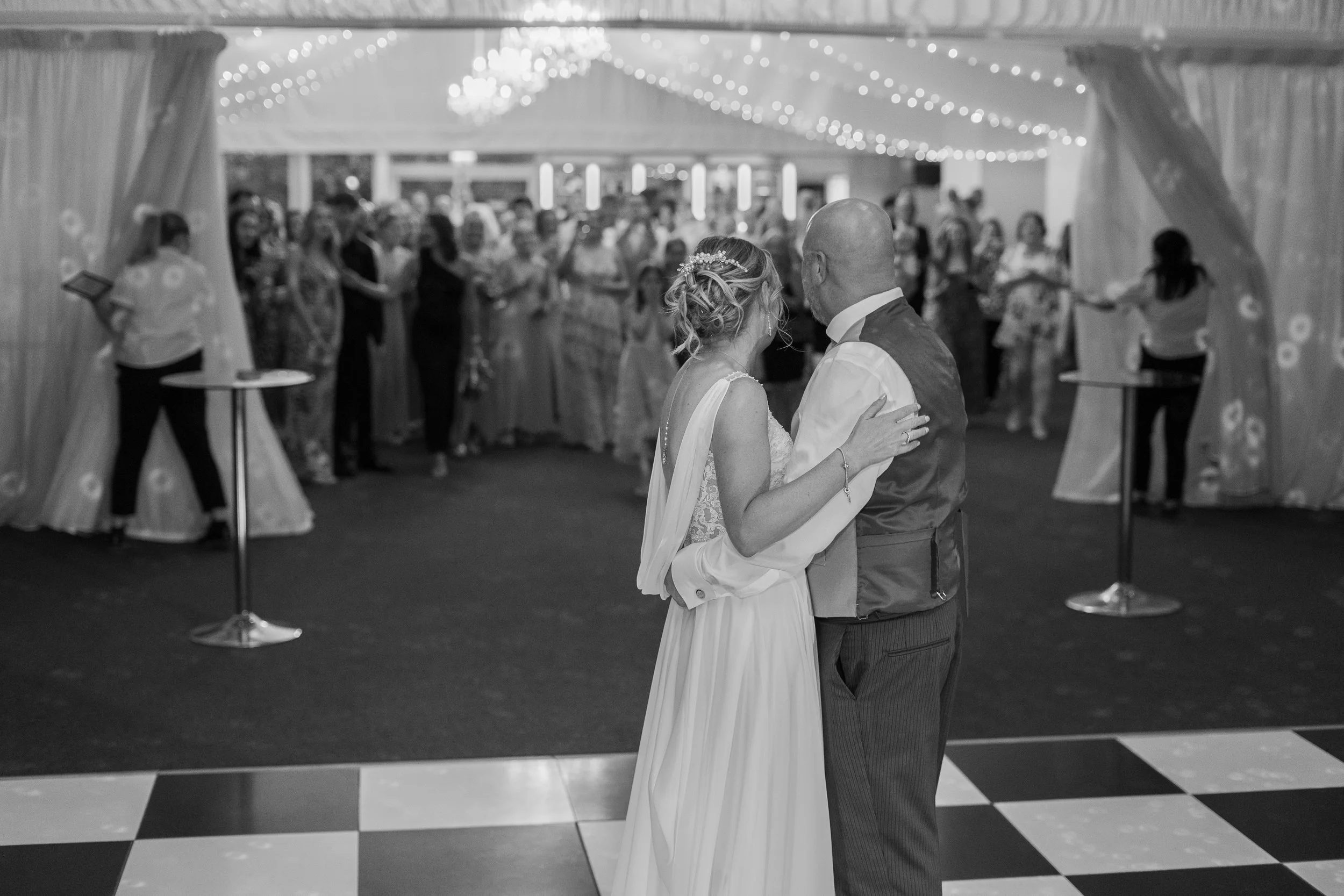 A bride and groom share their first dance at a wedding reception, with guests in the background.