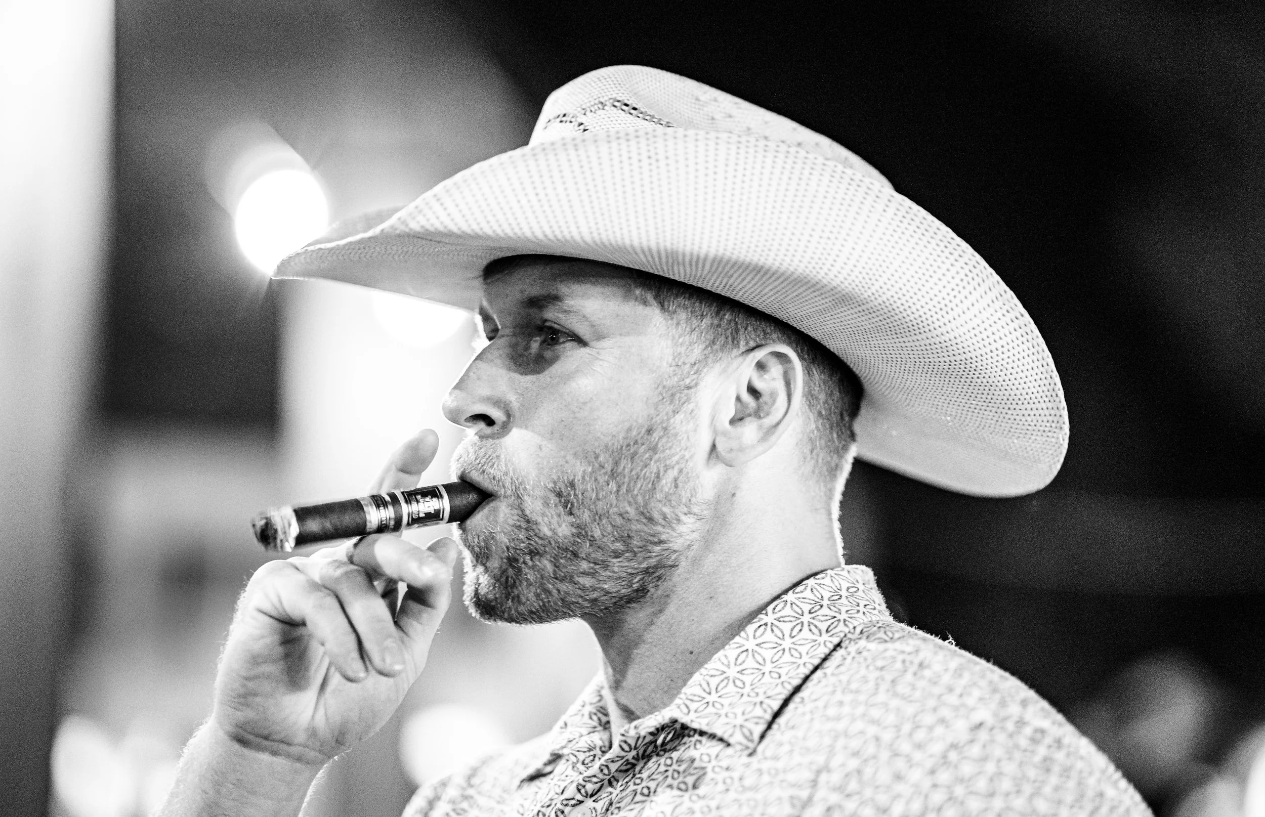 A man with a beard wearing a cowboy hat and patterned shirt, playing a wind instrument, possibly a clarinet, in a black-and-white photo.