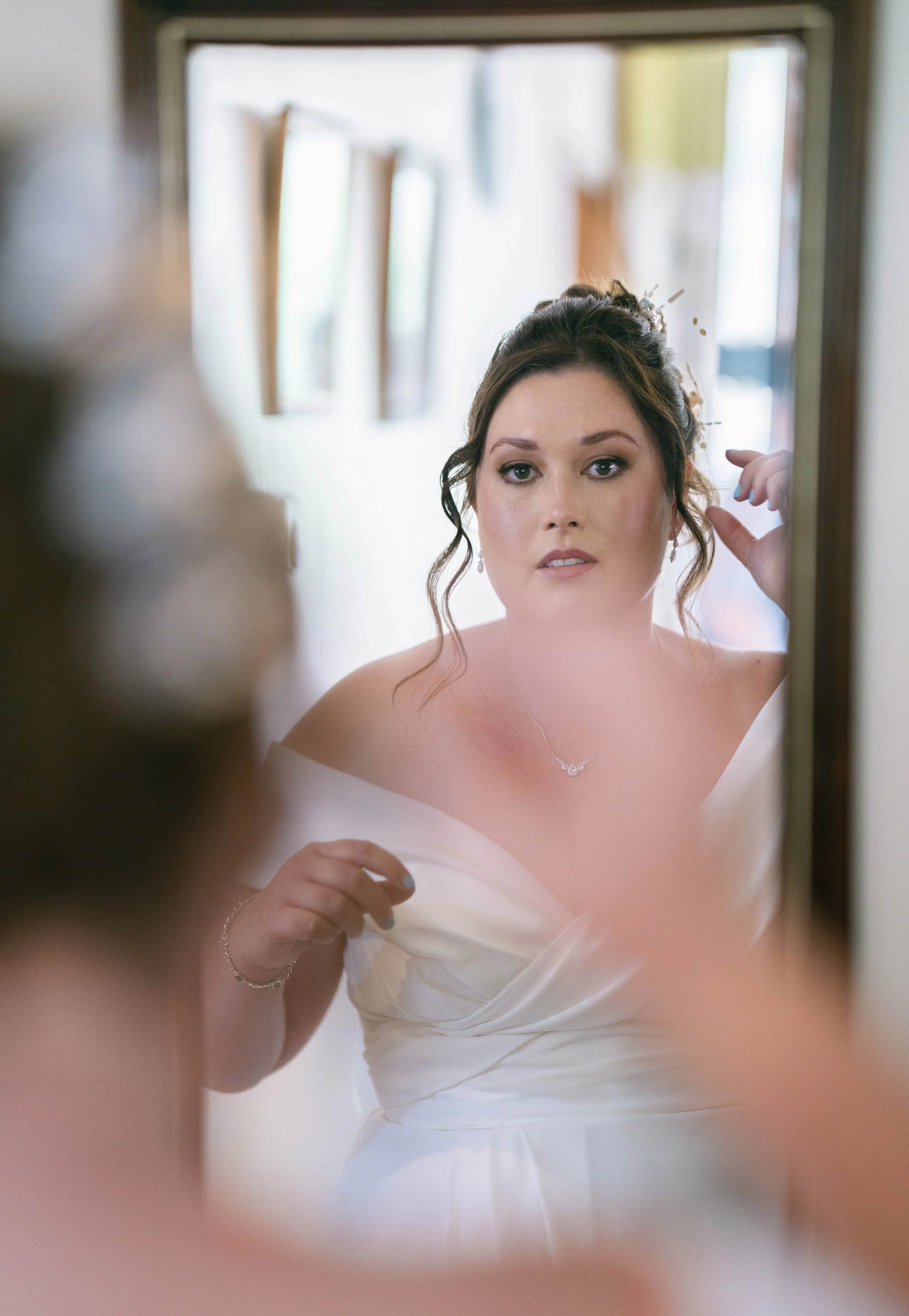 Brunette woman in a white dress looking at her reflection in the mirror, adjusting her hair.