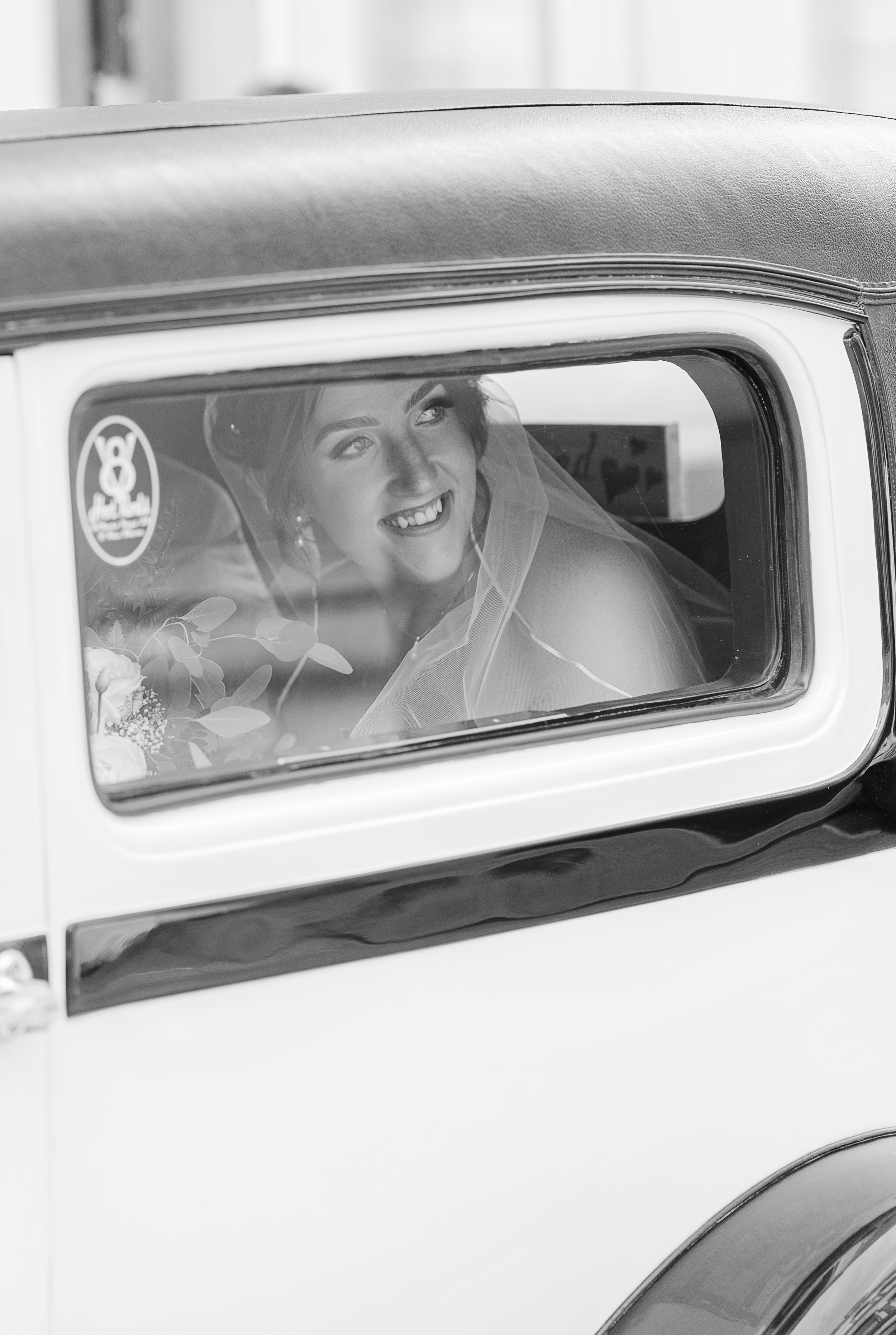 A smiling bride looking out of the window of a vintage car.