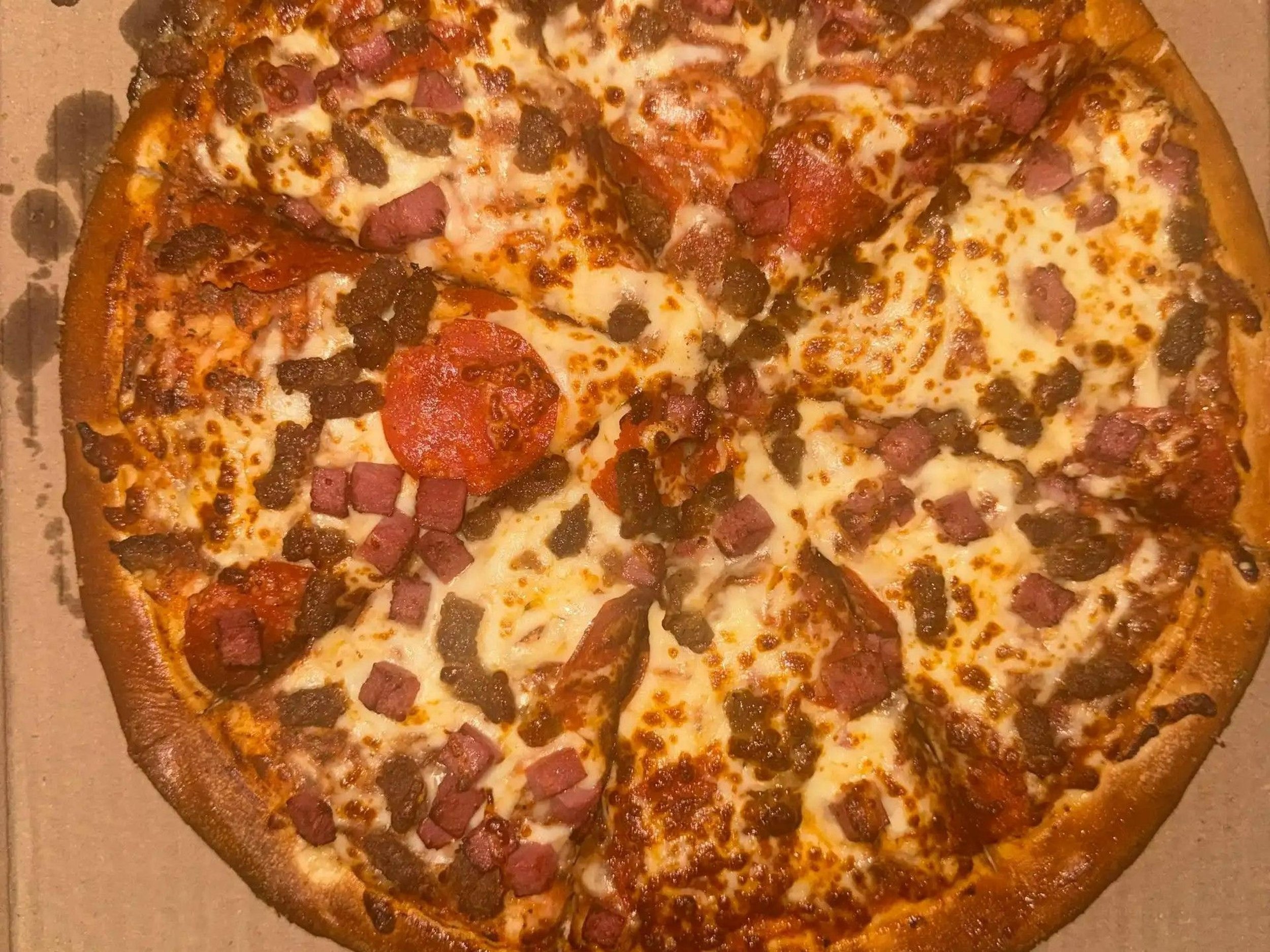 A pizza with cheese, pepperoni, sausage, diced ham, and bell peppers.