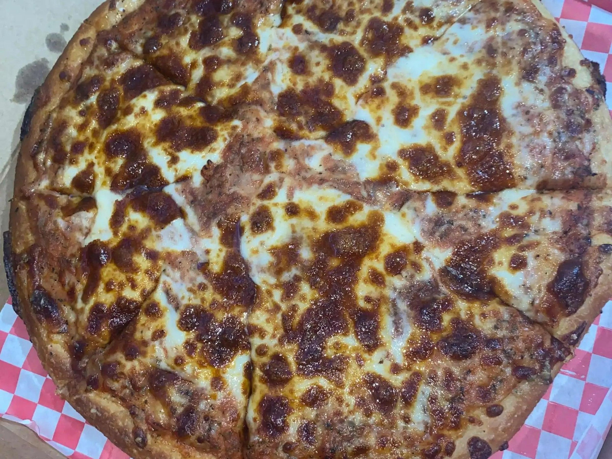 A large cheese and pepperoni pizza with a golden-brown crust, sitting on a red and white checkered paper.