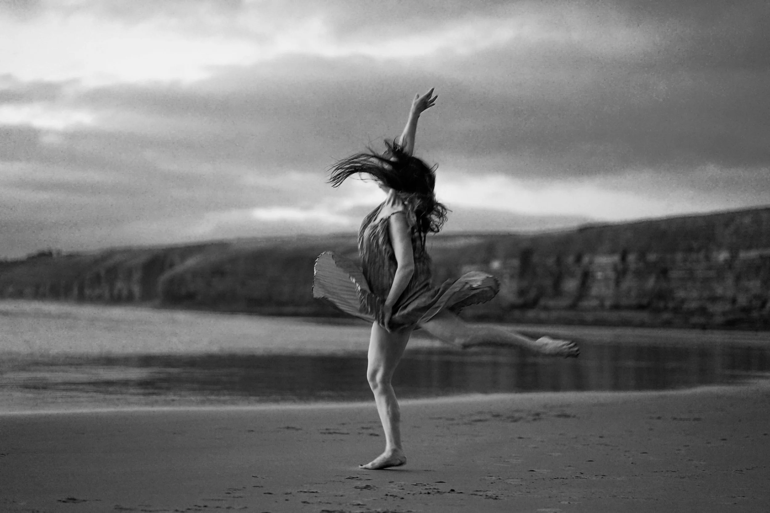 Fine art portrait of a woman dancing in a light dress on the beach in South Wales, Ogmore-by-Sea, landscape female photography.