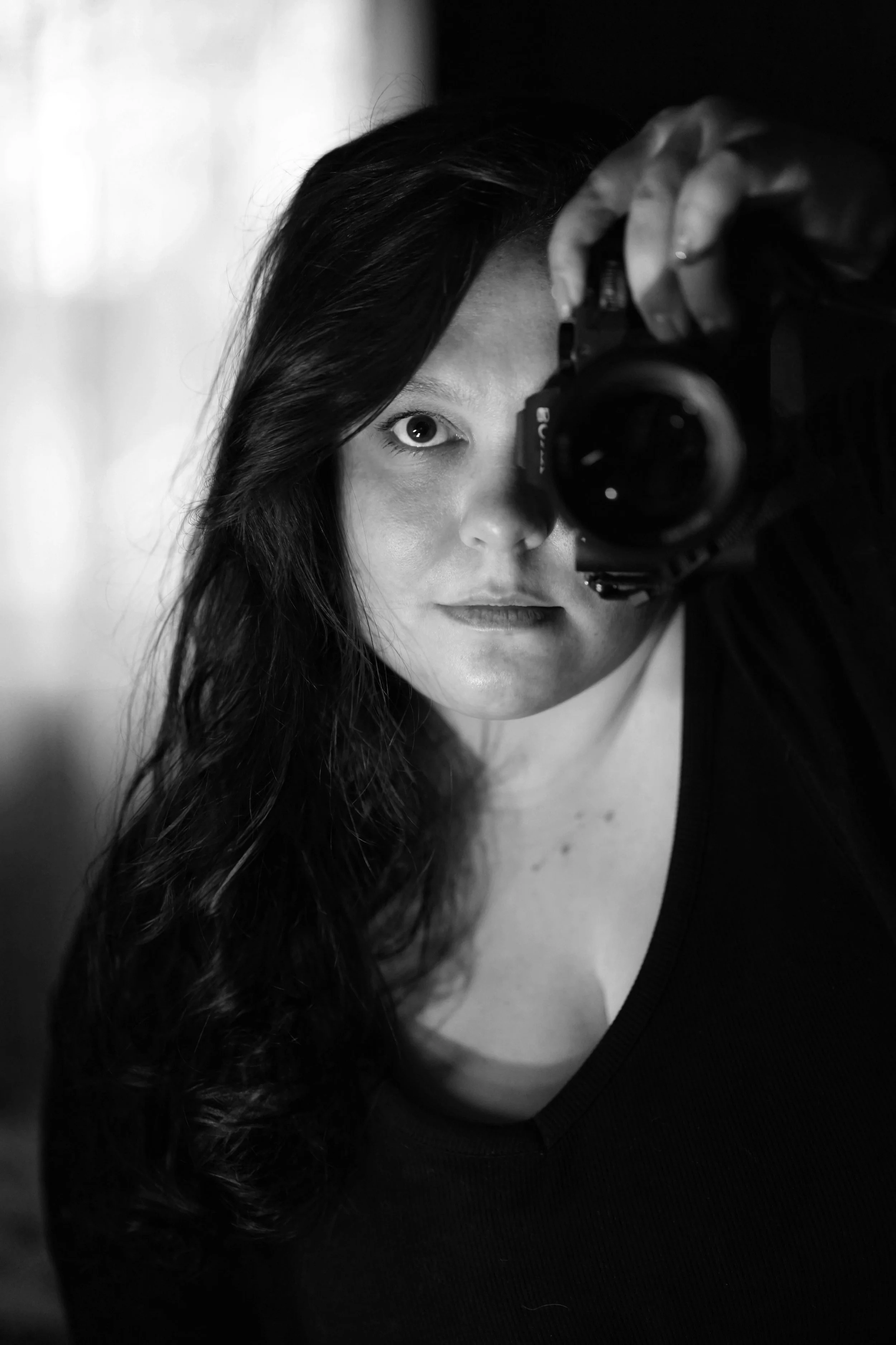 A woman with long dark hair taking a black and white selfie using a camera, photography Bridgend, South Wales.
