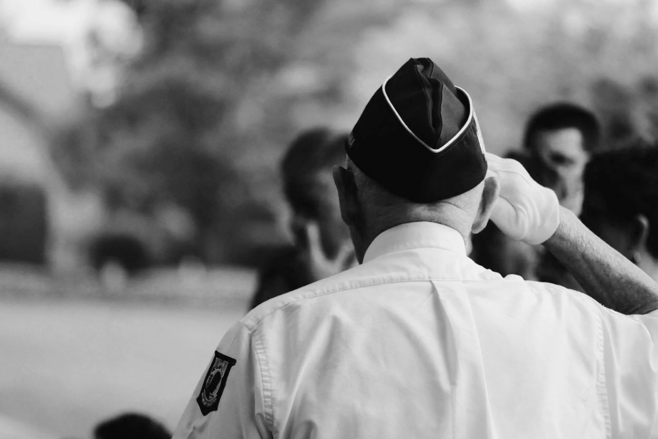 A person in a white martial arts uniform with a patch on the shoulder, holding their head with one hand, in a black-and-white photo, possibly during a martial arts class or event.
