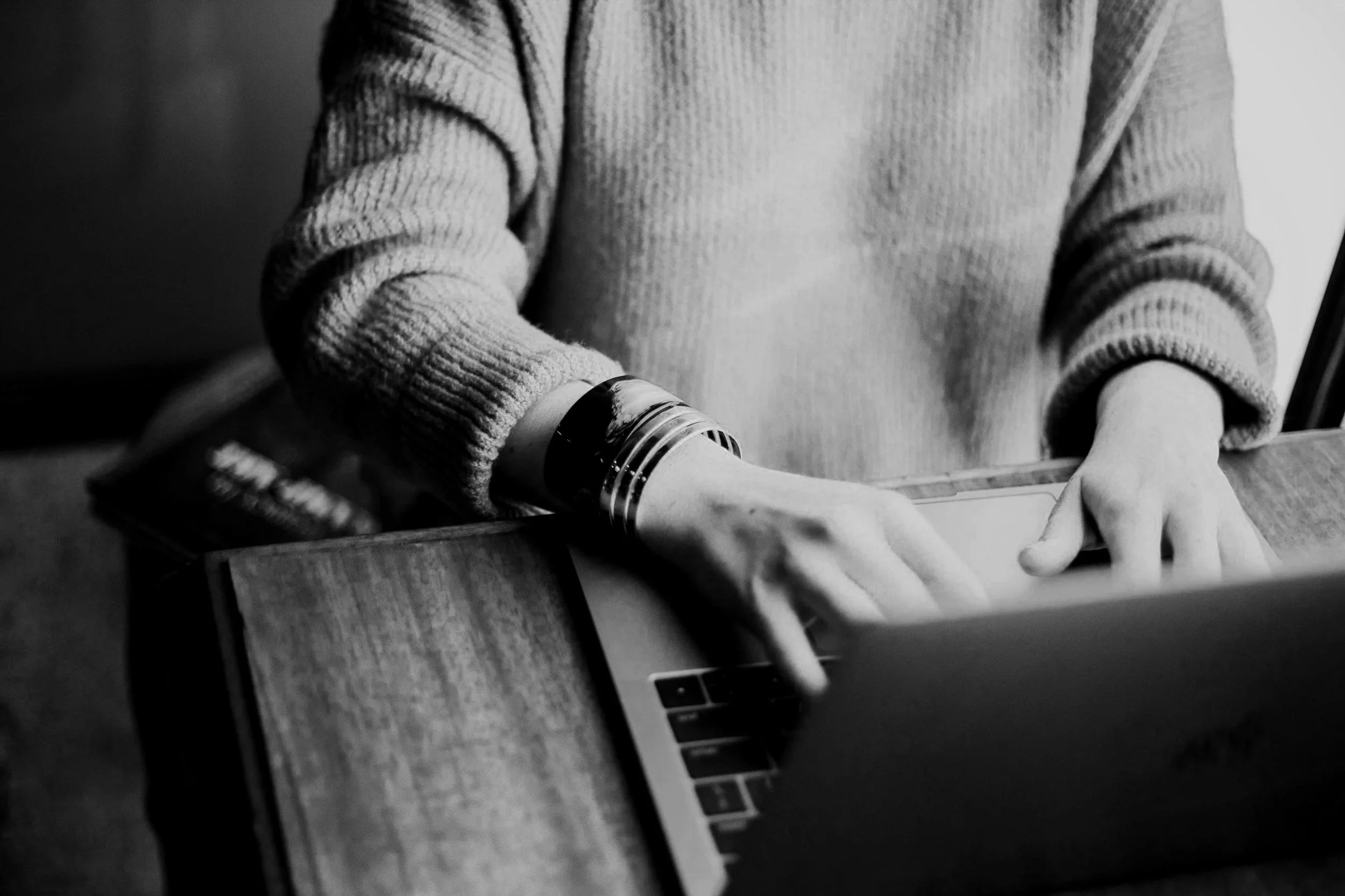 A person wearing a thick, textured sweater is placing a piece of paper into a slot on a laptop.