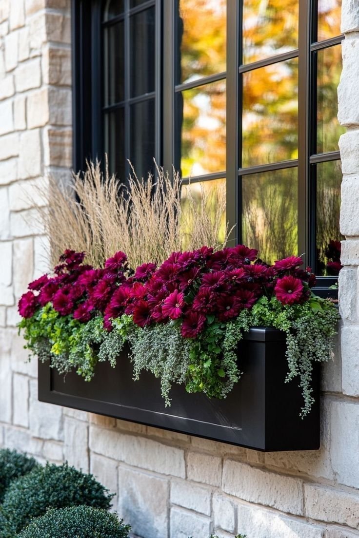 Window flower box with pink and white flowers, ornamental grasses, on a brick house wall.