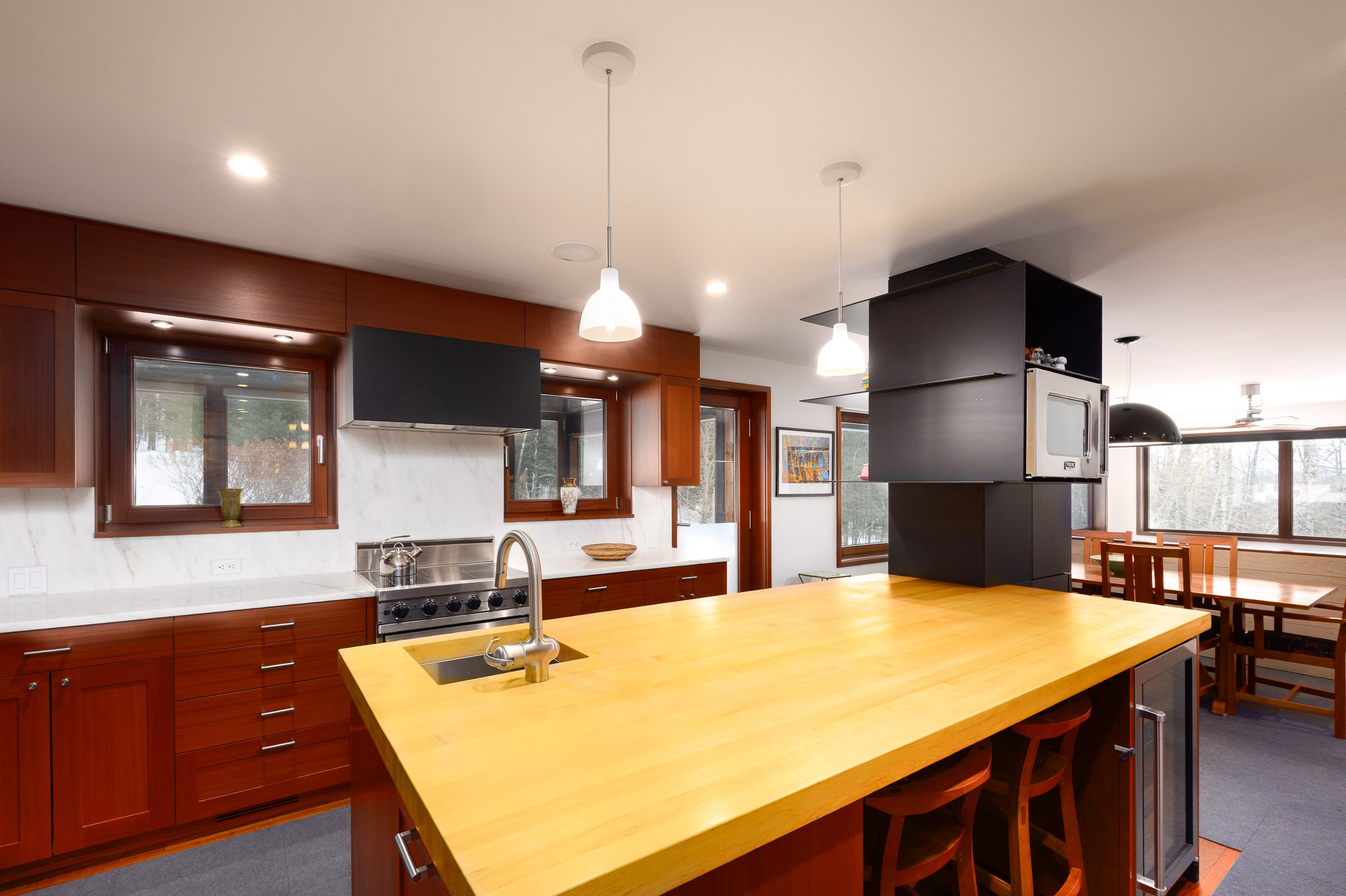 Modern kitchen with wooden cabinets, a large yellow island, and multiple windows showing a snowy outdoor scene.