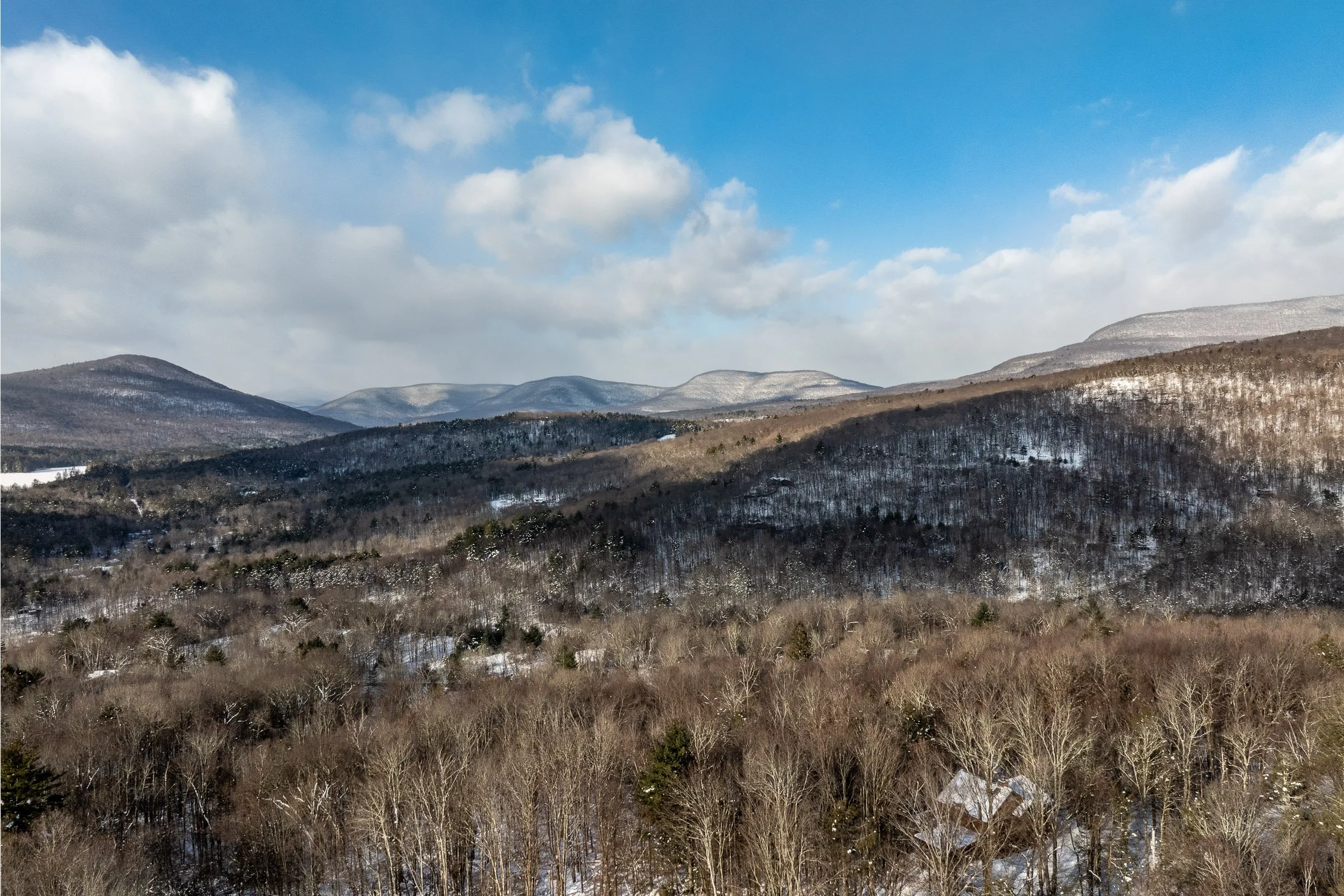 Snow-covered hills and mountains with a partly cloudy sky.