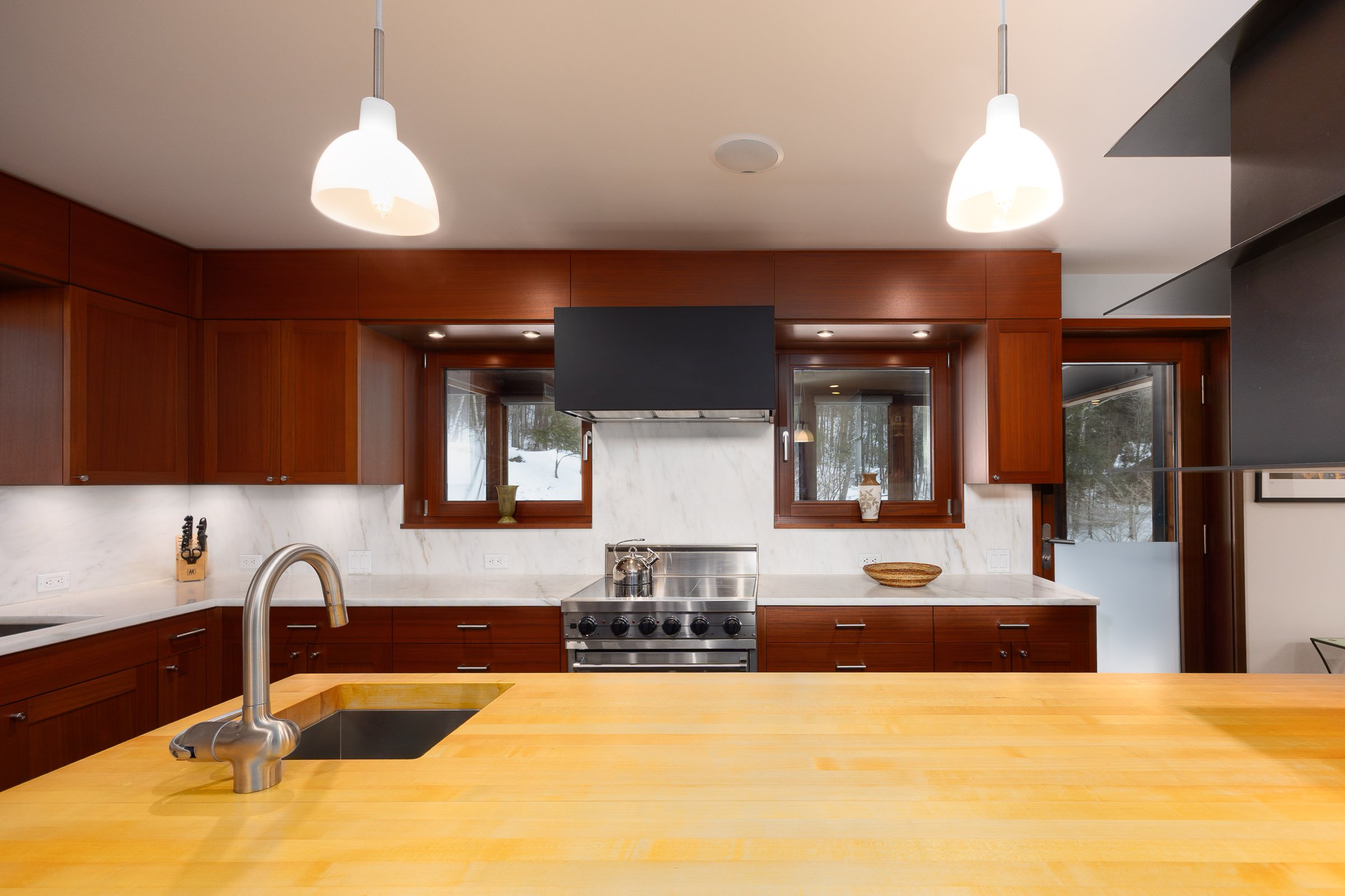 Modern kitchen with wooden cabinets, stainless steel stove, marble backsplash, and a large wooden island counter with a sink.