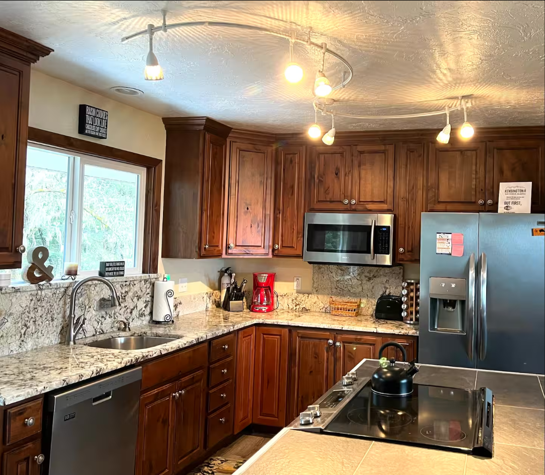 Kitchen with wooden cabinets, granite countertops, stainless steel appliances including a microwave, refrigerator, and dishwasher. There is a window above the sink, and various small appliances and decor items on the counters.