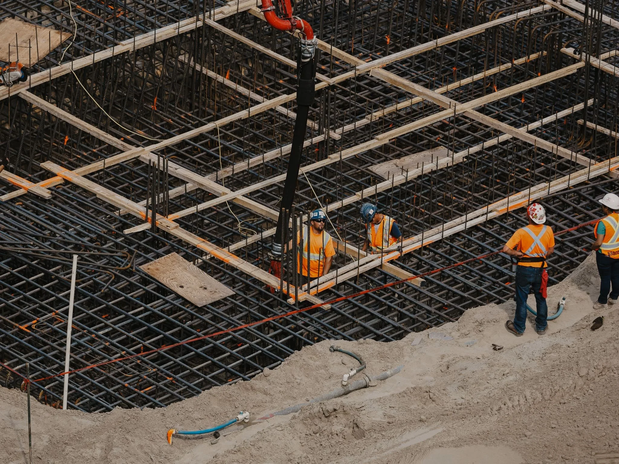 Travailleurs de la construction portant des casques et des gilets de sécurité orange, travaillant sur une structure en acier avec un réseau de treillis, à un site de construction.