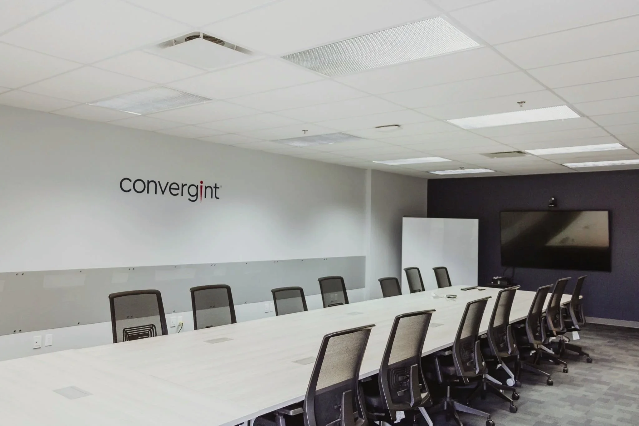 Salle de réunion avec une grande table, des chaises ergonomiques et un écran plat mural, avec un logo 'convergint' sur le mur gauche.