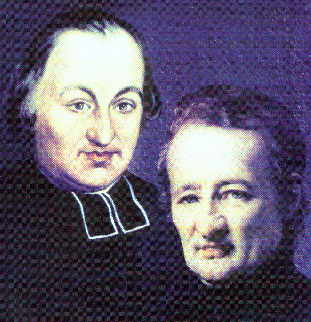 Portrait of two men with white shirts and dark clothing, standing close together against a dark background.