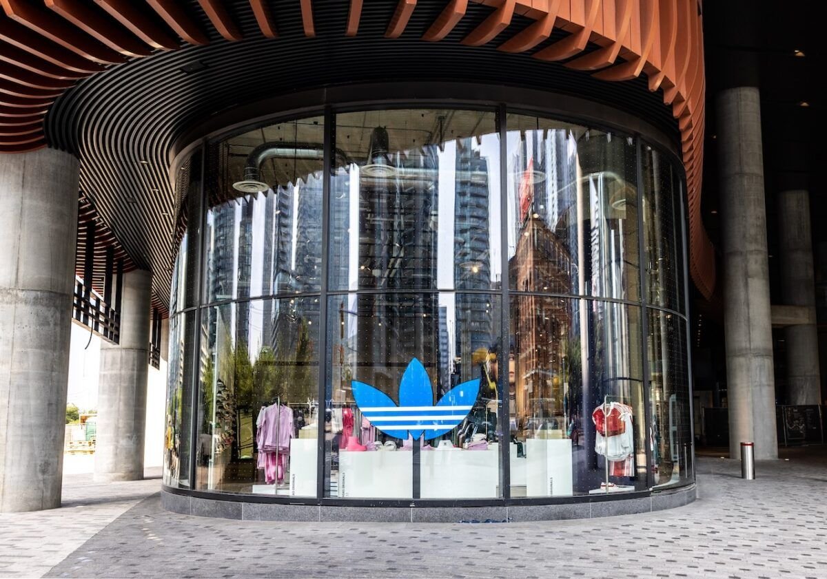 Modern retail store with curved glass exterior displaying clothing and a blue Adidas logo.