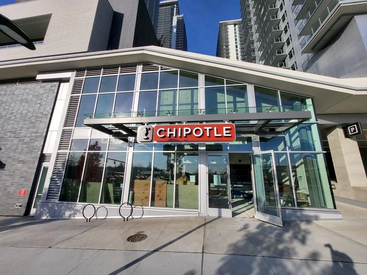 Exterior view of a Chipotle restaurant with a glass facade in an urban area with tall buildings