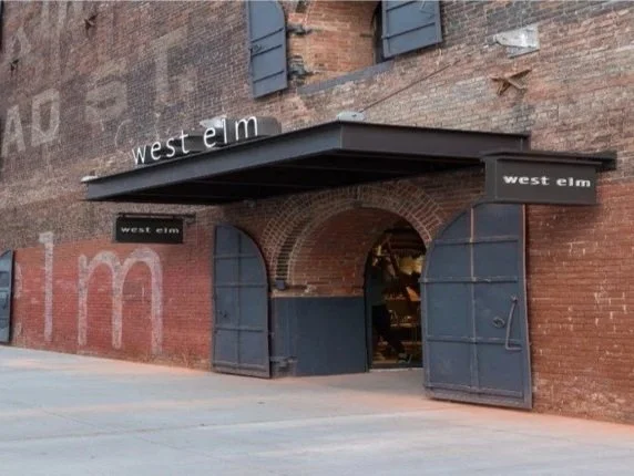 Exterior of a brick building with black metal double doors and a black awning, displaying the sign 'West Elm'.