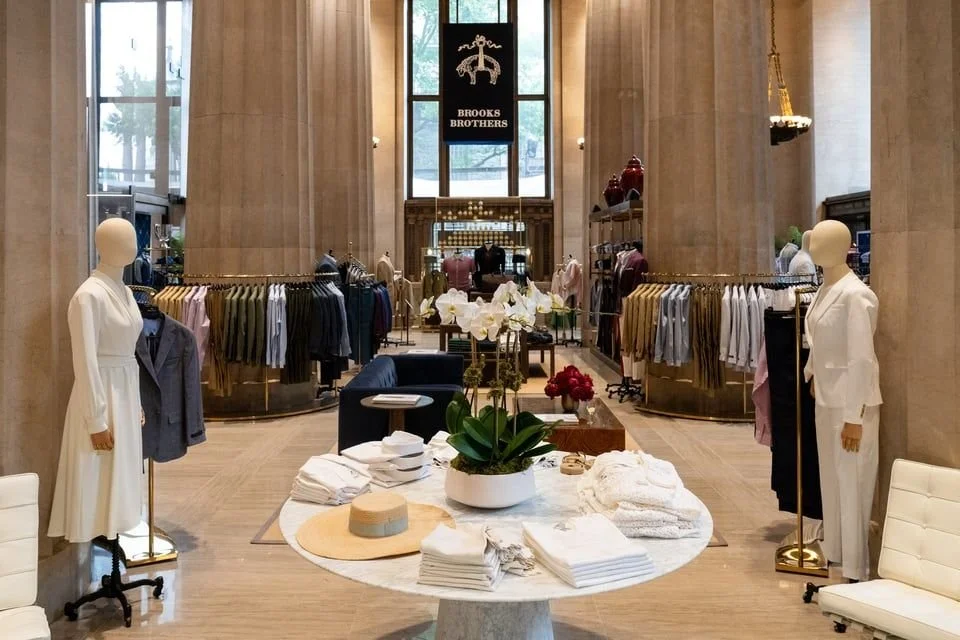 Interior of Brooks Brothers store with mannequins, clothing racks, and flower arrangements.