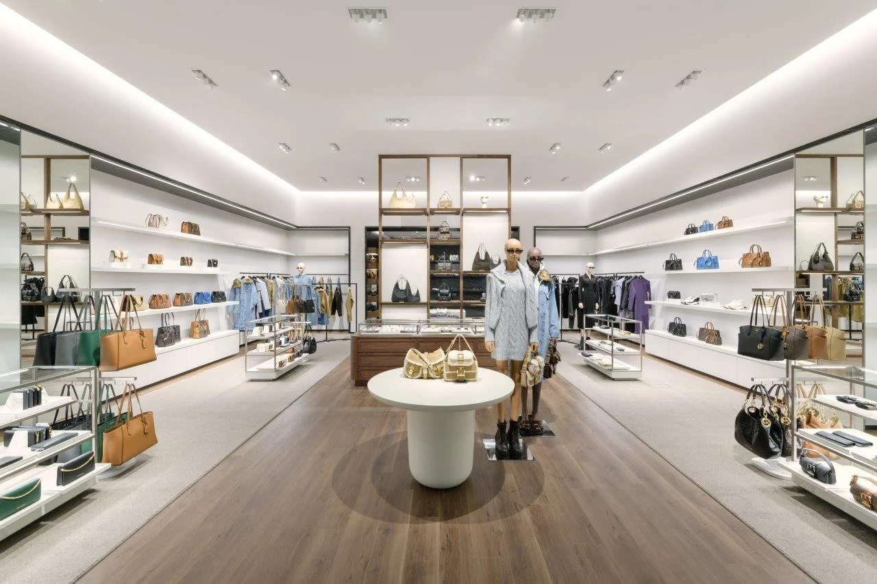 Interior of a luxury clothing and accessories store with mannequins wearing outfits and shelves displaying handbags and accessories.