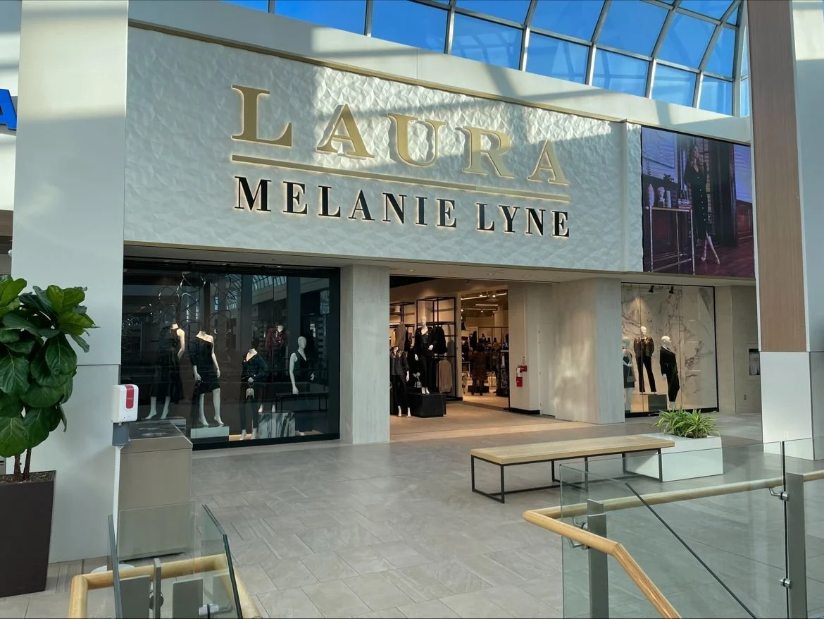 Storefront of Laura Melanie Lyne with mannequins in window display and an open entrance in a mall with glass ceiling