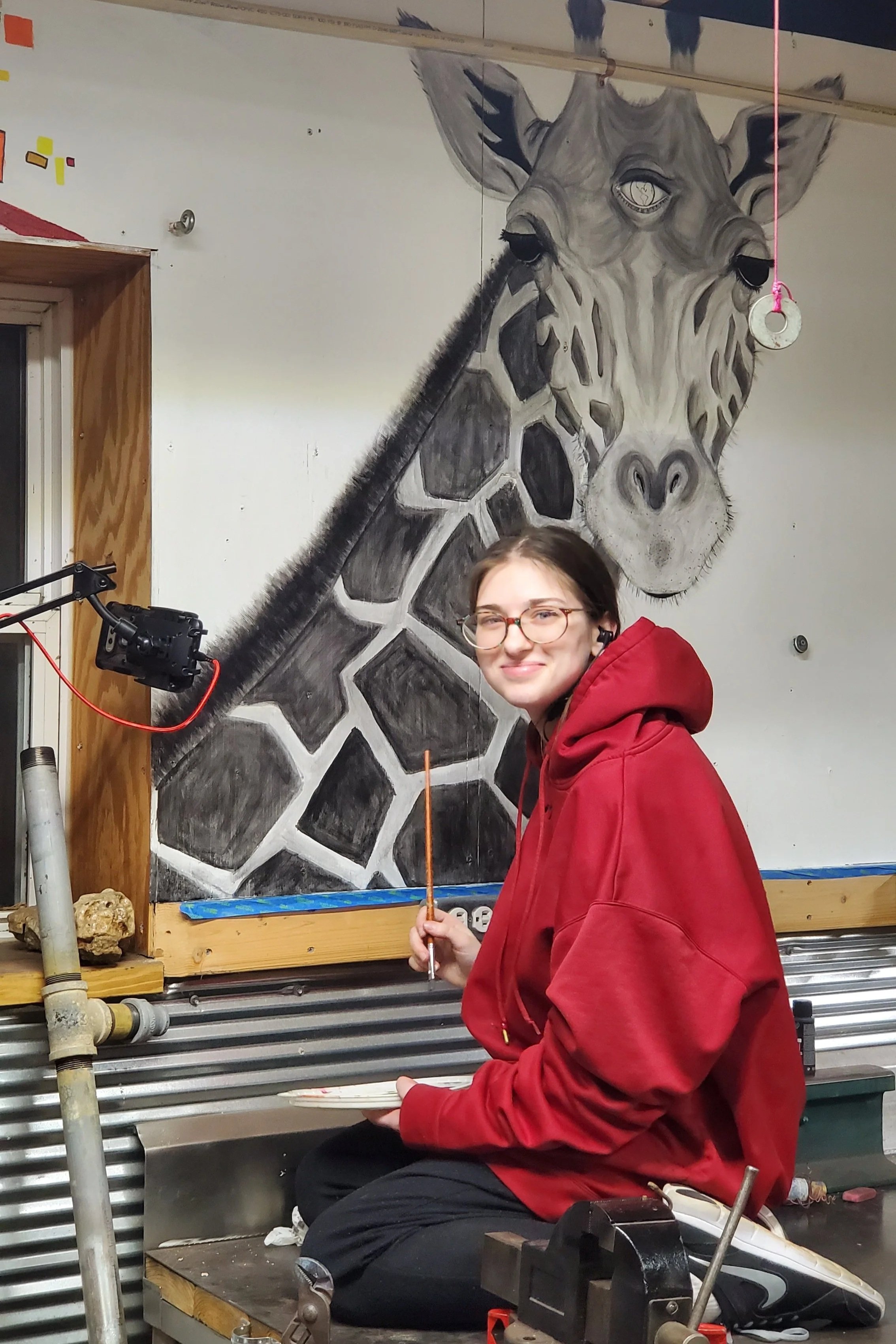 Studio artist Cierra Jayne painting large-scale giraffe wall mural at Refreshing Art Studio
