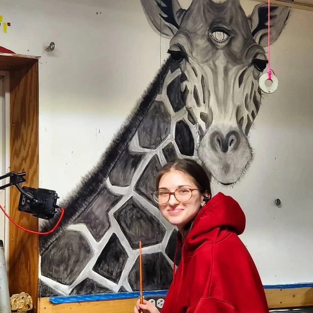 Cierra Jayne standing next to hand-painted giraffe wall mural