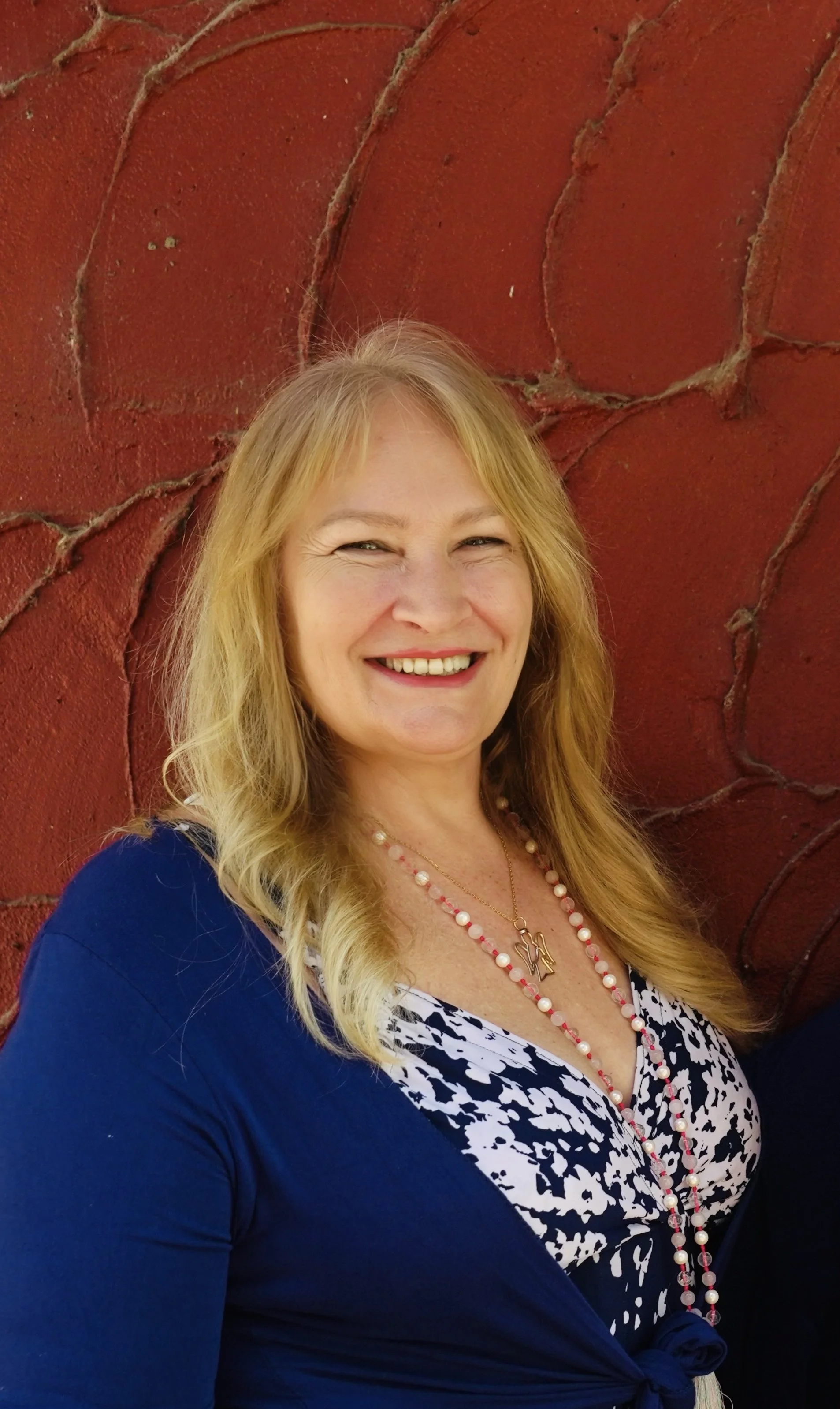 Portrait of a woman with blonde hair smiling against a red textured wall background.