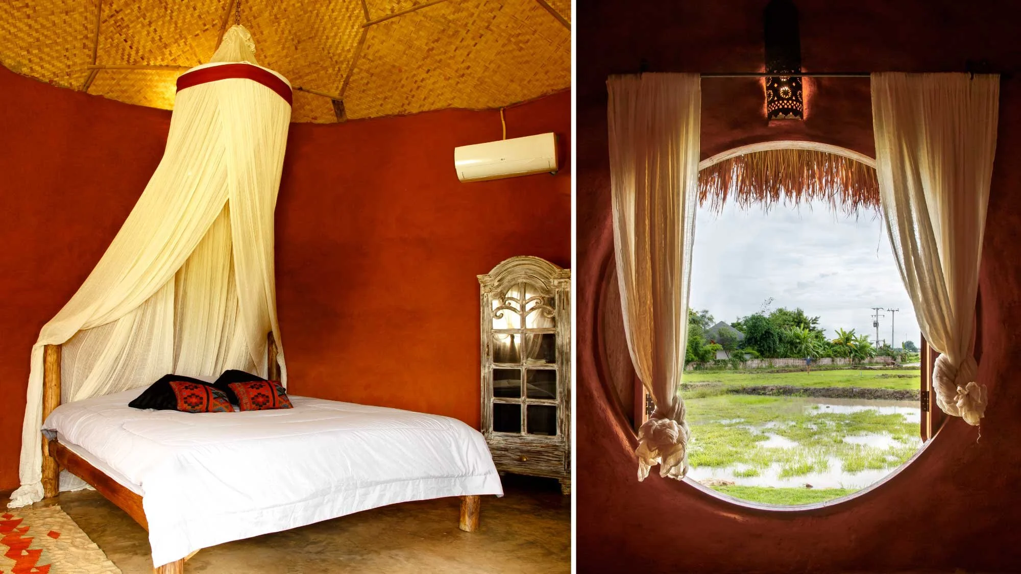 A bedroom with a rustic wooden bed, cream-colored canopy, red-orange textured wall, wooden ceiling, an air conditioning unit, and a window with curtains and a view of green fields and trees.