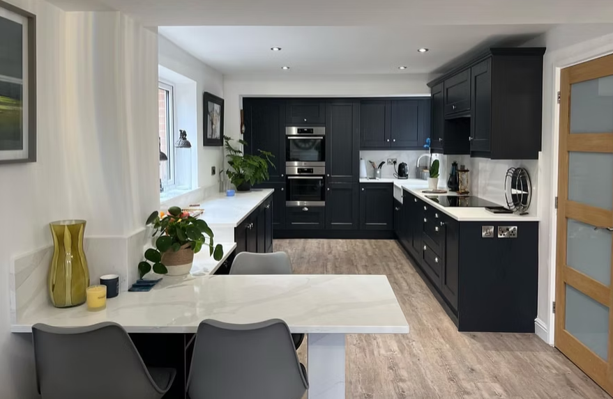 Modern kitchen with black cabinets, white countertops, and wooden flooring, featuring a dining area with a white table and gray chairs.