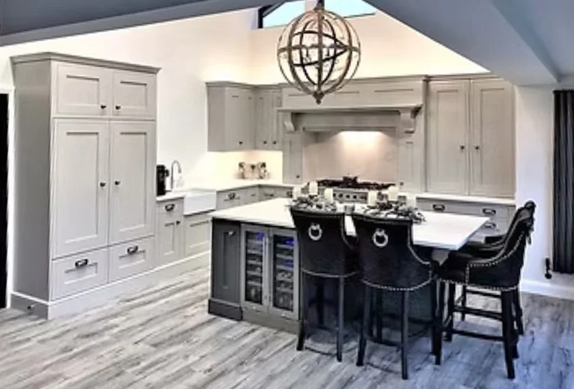 Modern kitchen with light gray cabinets, white countertops, a central island with black chairs, and a spherical chandelier.