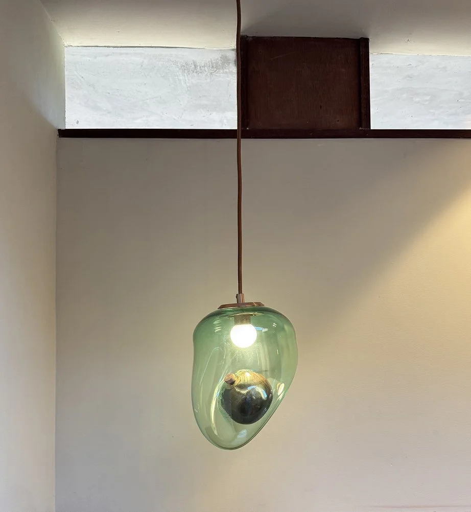 A hanging light fixture with a green glass shade and an exposed bulb, featuring a small, round black object inside the shade.