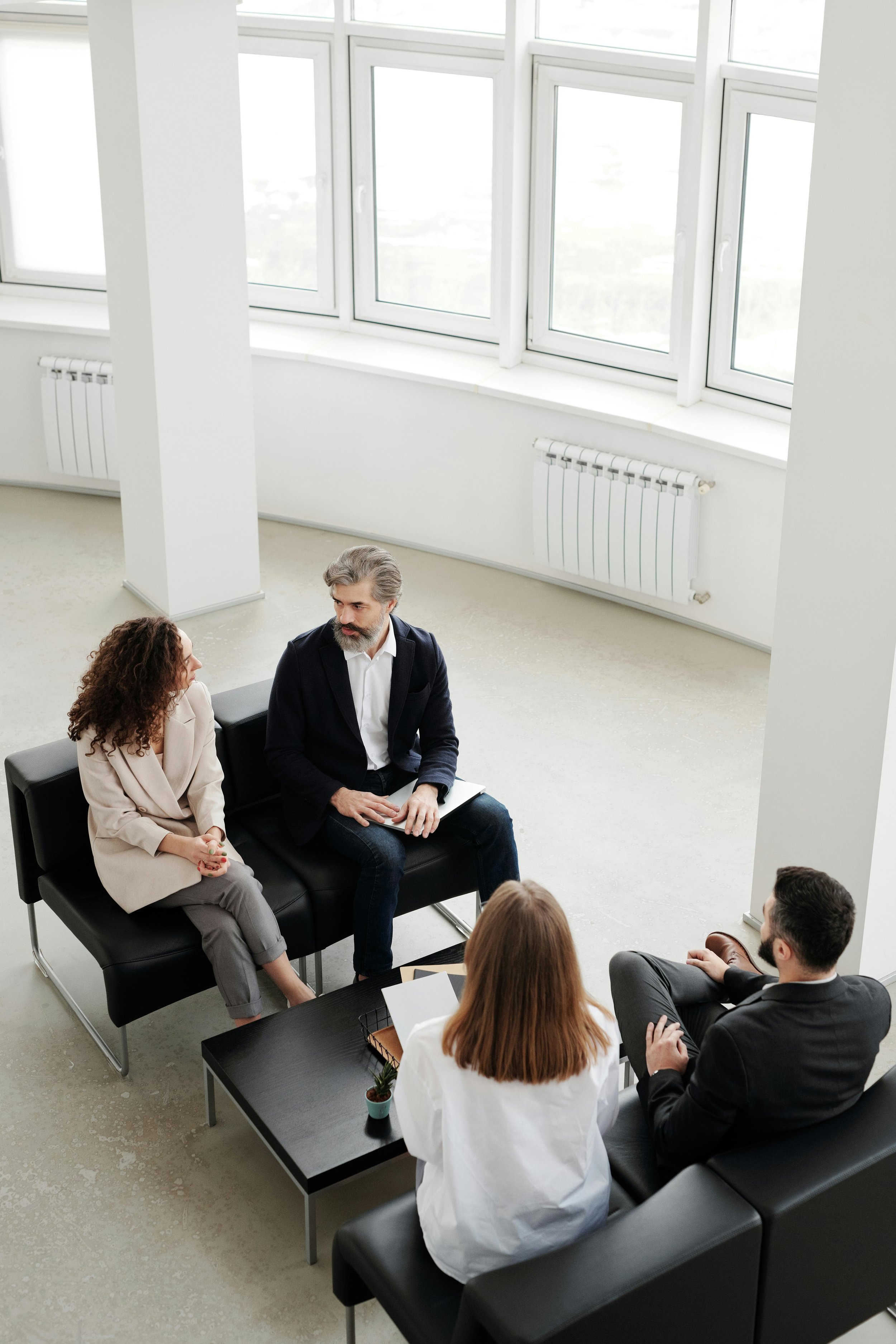 A group of four people having a discussion in a bright, modern office with large windows and minimal decor.
