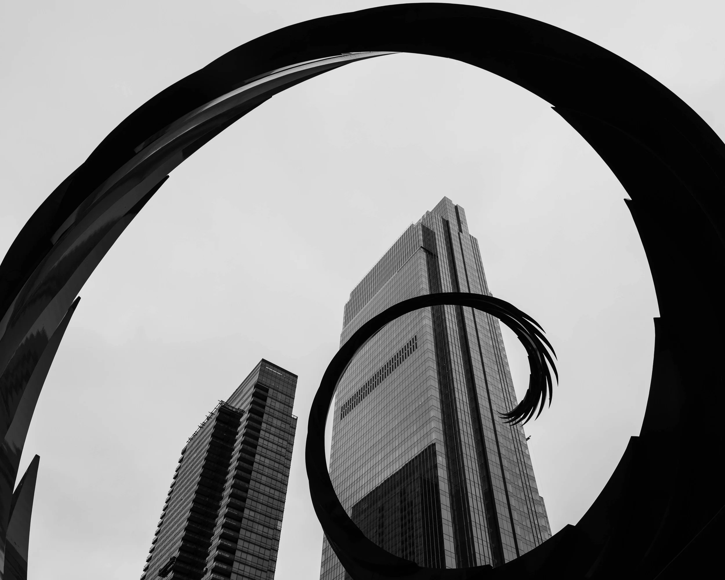 Black and white photo of tall skyscrapers viewed through a spiraling architectural structure.