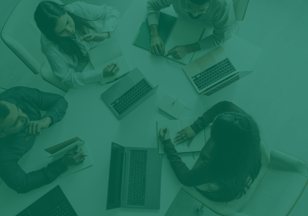 Four people sitting around a table with laptops and notebooks, engaged in a discussion.