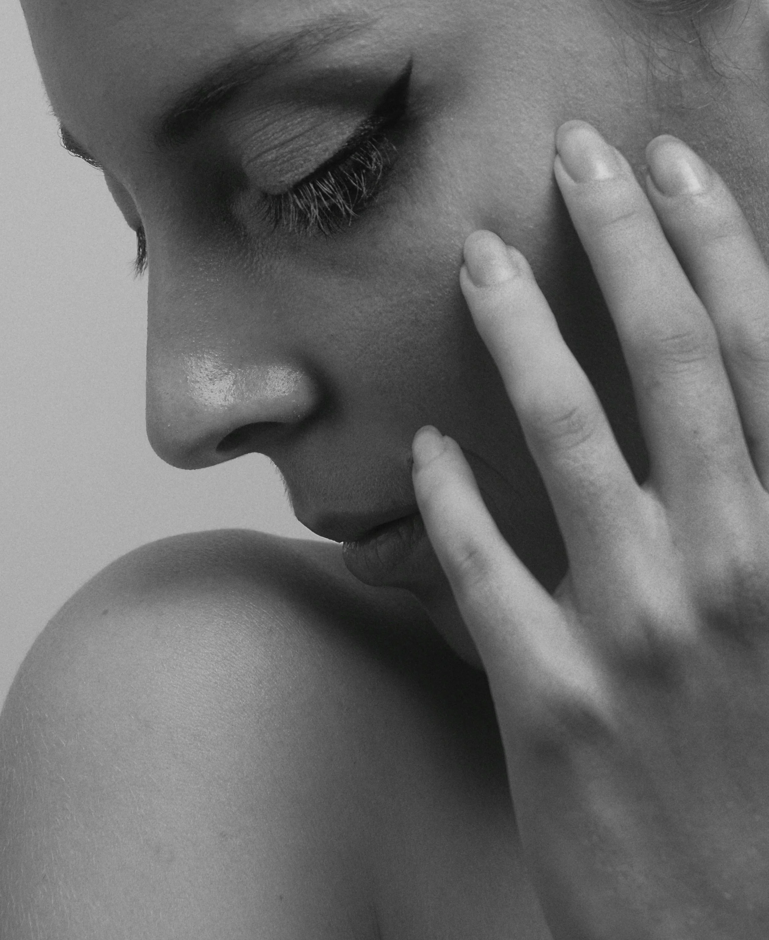 Close-up black and white photo of a woman with closed eyes touching her face with her hand.