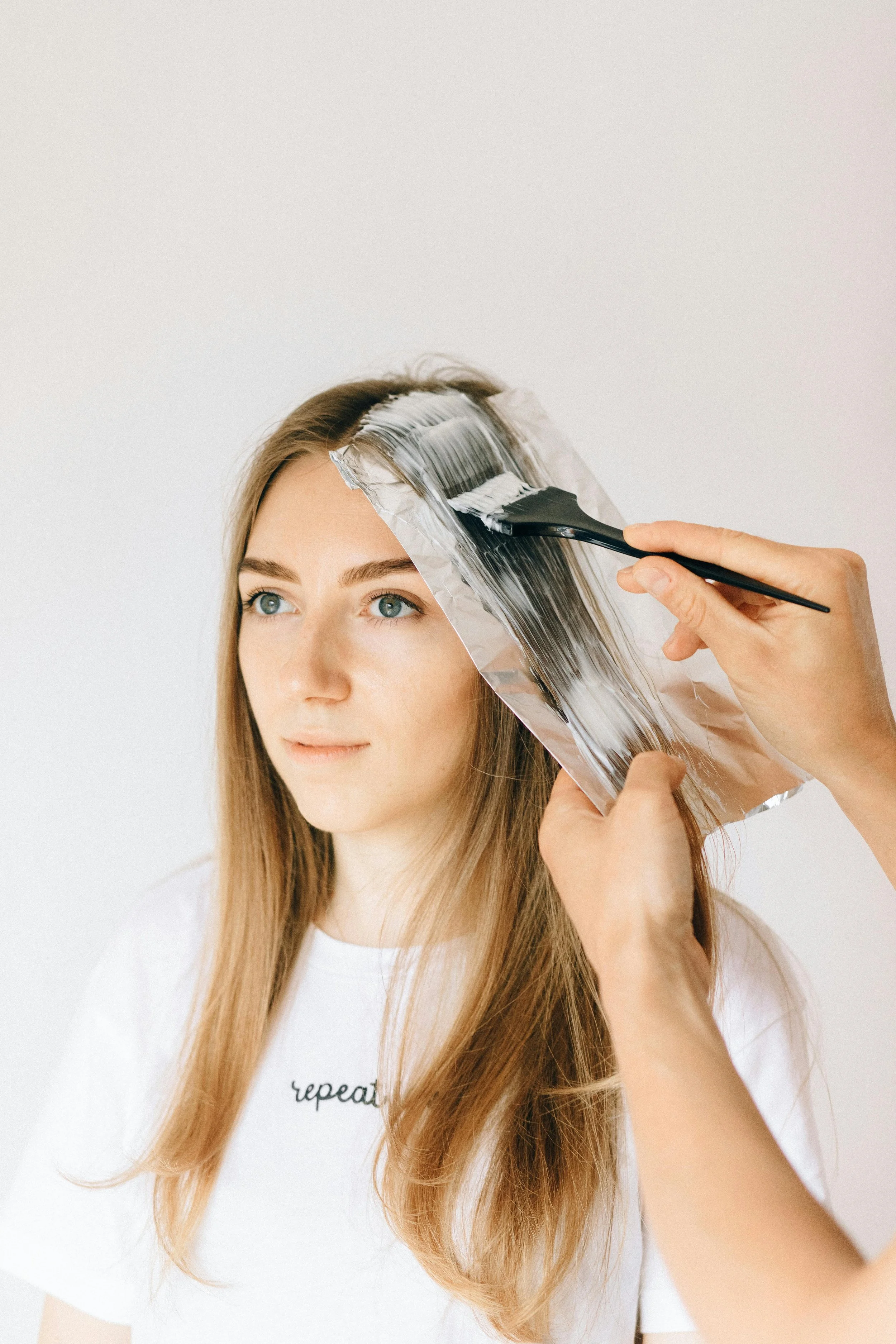 A woman is getting her hair colored using foil and a brush, with a stylist applying hair dye or bleach.