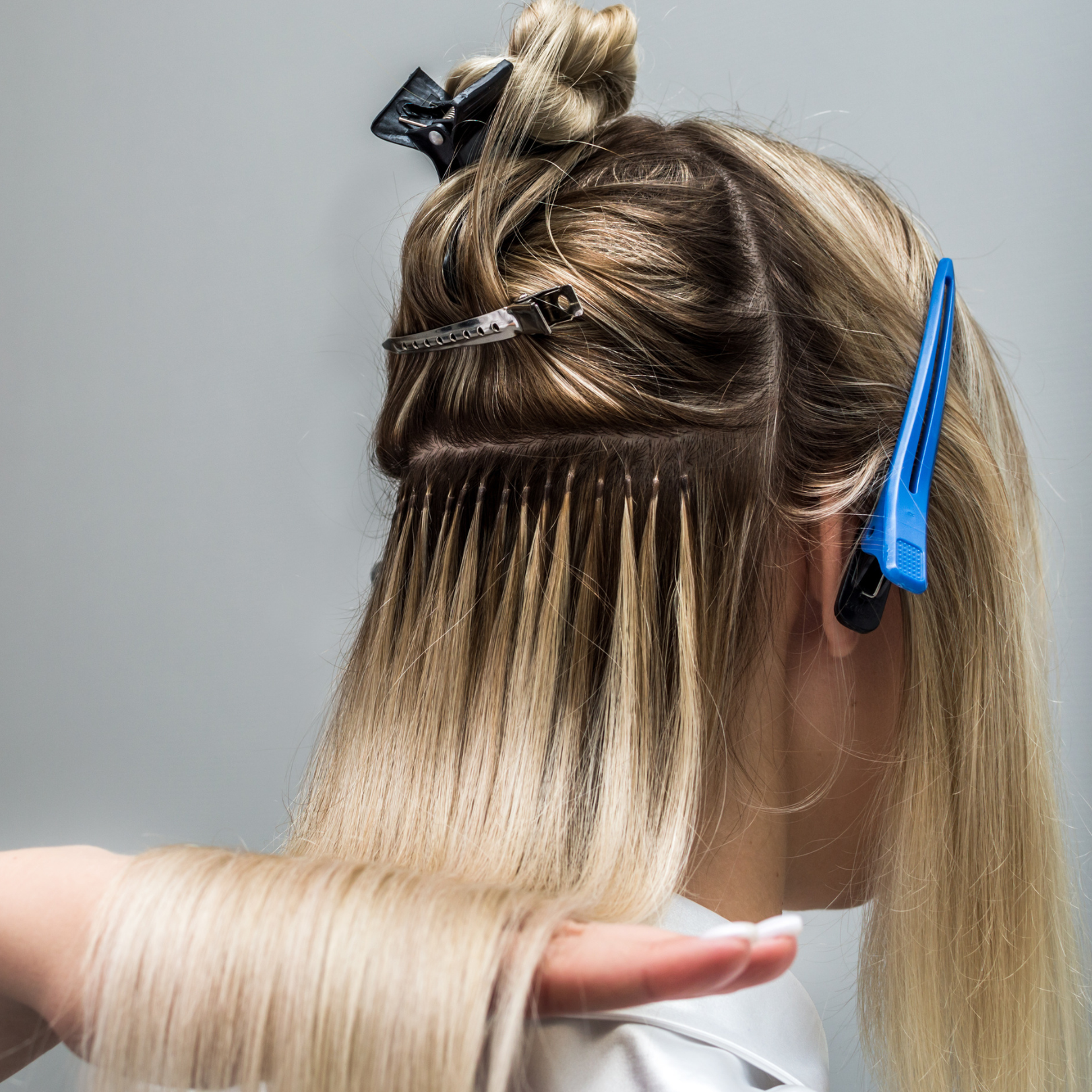A person getting their hair cut or styled, with hair clips and a section of hair lifted, and a hand holding a section of hair.